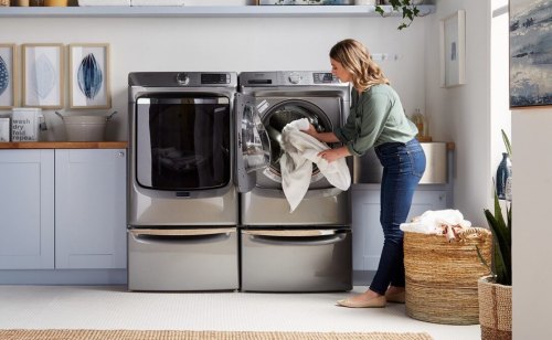 Person loading clothes into gray Maytag® front load washer and dryer pair on pedestals